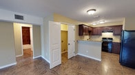 This single-floor space offers a practical and well-organized layout designed for comfortable everyday living. The kitchen is a standout feature, showcasing rich dark wood cabinetry that provides ample storage, complemented by light granite-style countertops that offer a clean contrast. A peninsula-style breakfast bar extends from the main counter, creating a natural divide between the kitchen and the surrounding living area while offering additional prep and seating space. Black appliances, including a range, add a cohesive, modern touch to the kitchen's aesthetic. The flooring throughout is a durable tile in a warm earth tone, lending consistency and easy maintenance across the space. Flush-mount ceiling fixtures provide steady, even lighting throughout. A pair of classic paneled white doors leads to a utility or laundry area, accented by a warm yellow interior that adds a pop of color. The open doorway to an adjoining room suggests a flowing, connected floor plan that encourages ease of movement throughout the home. White trim and baseboards frame each room neatly, while the neutral wall tones create a bright, welcoming ambiance suitable for a variety of interior styles.