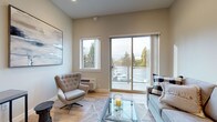 This single-floor unit showcases a thoughtfully designed open-concept layout that seamlessly connects the kitchen, dining, and living areas. The kitchen is outfitted with stainless steel appliances — including a gas range, built-in microwave, French door refrigerator, and dishwasher — complemented by light wood cabinetry, white quartz countertops, and light hardwood-style flooring. A central island with bar seating provides additional workspace and casual dining. A stacked washer and dryer unit is conveniently integrated near the kitchen entry.

The living area benefits from generous natural light streaming through a large sliding glass door and an adjacent window, both offering outdoor views of surrounding greenery. The space features elevated ceilings that enhance the sense of openness, with recessed lighting throughout.

Two bedrooms offer comfortable accommodations, each with soft carpeting, neutral tones, and ample closet space. One bedroom features a large window with an outdoor view, while the other includes a built-in closet with sliding doors.

The bathroom is finished with light wood cabinetry, a wide vanity with a quartz countertop, a large wall mirror, and tile-style flooring, contributing to the unit's clean and contemporary aesthetic throughout.
