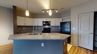 This single-story residence on Hayes Court in Beavercreek, Ohio offers a well-designed, open-concept layout with thoughtful finishes throughout. The kitchen serves as a central feature, showcasing white upper cabinetry, dark lower cabinets, a gray subway tile backsplash, black appliances, and a generously sized island topped with granite countertops. Pendant lighting and a track light system illuminate the space, which flows seamlessly into the main living area. The living space features rich hardwood-style flooring and a built-in desk nook, adding functional character to the open layout. Sliding glass doors lead to a private balcony, filling the space with natural light and offering outdoor views. The bedrooms are carpeted for comfort and include multiple windows dressed with blinds; one room features a ceiling fan. Bathrooms are finished with granite vanity tops, tile flooring, and gray cabinetry—one includes a walk-in glass shower, while the other offers a soaking tub with tile surround. A dedicated laundry room with full-size washer and dryer hookups adds everyday convenience. The overall palette of neutral grays, warm wood tones, and stone finishes creates a cohesive, modern ambiance throughout.