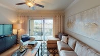 This single-floor residence offers a thoughtfully designed layout with multiple living areas that balance functionality and style. The kitchen is outfitted with dark espresso cabinetry, light stone countertops, a white subway tile backsplash, and a full suite of stainless steel appliances, including a French door refrigerator, electric range with over-the-range microwave, and dishwasher. A separate pantry provides additional storage. The adjacent dining area features hardwood-style flooring, crown molding, track lighting, and large arched mirrors that enhance the sense of space. The living room is bright and open, with sliding glass doors leading to a private balcony, ceiling fan, and crown molding details. Two bedrooms each feature plush carpeting, ceiling fans, generous natural light from large windows with blinds and drapery, and ample space. Both bathrooms include arched tub-shower combinations with tile surrounds and dark vanity cabinetry with stone-topped counters. A dedicated laundry room houses a full-size washer and dryer alongside additional shelving, completing this well-rounded residence.