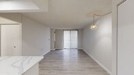 This thoughtfully updated 2-bedroom, 1-bathroom unit makes efficient use of its single-floor layout, offering a clean, modern aesthetic throughout. Light wood-look flooring flows consistently across the living, dining, and bedroom areas, complementing the neutral grey-and-white color palette.

The open-concept kitchen is a standout feature, finished with high-gloss white cabinetry, a striking marble-veined quartz countertop and island, white tile backsplash, and a full suite of stainless steel appliances including a range, over-the-range microwave, dishwasher, and refrigerator. Recessed lighting keeps the space bright and functional.

The combined dining and living area is open and airy, anchored by a full-height sliding glass door with vertical blinds that floods the room with natural light. A stylish woven pendant light adds a warm, decorative touch.

The primary bedroom is generously proportioned, featuring a walk-in closet with built-in shelving, a pendant light fixture, and a large window with vertical blinds. The second bedroom also benefits from a sizable window and ample wall space.

The bathroom is finished in crisp white with light tile flooring, a single vanity with under-sink storage, a wall mirror, and a full bathtub with shower. A hallway connects all rooms, completing this well-organized and move-in-ready unit.