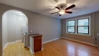Located at 5541 S Everett Ave in Chicago's vibrant Hyde Park neighborhood, this single-floor unit offers a well-organized and functional layout throughout. The main living area is bright and welcoming, featuring warm hardwood flooring that extends throughout the entire space. A ceiling fan with a built-in light fixture anchors the room, providing both comfort and illumination. Natural light filters in through double windows, offering views of the surrounding neighborhood. A charming arched doorway connects the living area to the kitchen, adding an architectural touch that enhances the flow of the space. The kitchen is efficiently designed with wooden cabinetry, granite-style countertops, a stainless steel sink, and a full-size refrigerator — providing all the essentials in a compact, practical arrangement. A peninsula counter with built-in storage serves as a natural divider between the kitchen and living areas. The bedroom features generous closet space, including a large walk-in closet outfitted with full-length hanging rods, offering ample storage. Consistent hardwood flooring, neutral gray walls, and clean white baseboards create a cohesive and understated aesthetic throughout the unit, making it a functional and comfortable Chicago residence.