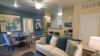 Located at 12801 Lafayette St in Thornton, Colorado, this single-floor residence offers a well-designed, open-concept layout that seamlessly connects the main living spaces. The living room is a welcoming centerpiece, featuring warm hardwood-style flooring, a ceiling fan, and a bold teal accent wall that adds a contemporary pop of color against the neutral beige walls. A comfortable seating area flows naturally into a dedicated dining space, making the layout ideal for both everyday living and entertaining. The kitchen is accessible via a raised breakfast bar with bar stool seating, providing a convenient pass-through that keeps the space feeling open and connected. White cabinetry and under-cabinet lighting give the kitchen a clean, functional aesthetic. Tasteful wall art and carefully chosen décor throughout contribute to a cohesive, modern ambiance. The overall design balances practicality with style, offering a comfortable and visually appealing living environment in the heart of Thornton, CO.