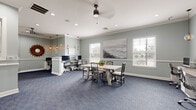 Located in Palm Coast, Florida, this single-floor office space offers a polished and functional environment designed for productivity and professionalism. The layout comprises a welcoming hallway and a spacious main office area, connected seamlessly by elegant French doors and wide doorways.

The hallway greets visitors with herringbone-patterned wood-look tile flooring, soft sage-green walls accented by crisp white trim and crown molding, and an interior pass-through window that adds a refined, boutique-office feel.

The main office is carpeted in a rich blue textured weave and features soft sage-green walls adorned with coastal artwork, including a large seascape canvas painting. Multiple workstations with built-in white cabinetry and dual monitors line the perimeter, while a central conference-style table with chairs provides space for meetings or collaboration. A seating area with two upholstered chairs offers a comfortable spot for client consultations. Natural light flows in through multiple windows fitted with white horizontal blinds, complemented by recessed ceiling lights, a ceiling fan, and warm pendant lighting. Crown molding and white wainscoting throughout add a refined architectural touch, creating a professional yet inviting atmosphere.