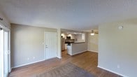 This single-floor space features an open-concept design that seamlessly connects the living area to the kitchen, creating a cohesive and functional layout. The living area is finished with warm hardwood-style flooring, transitioning to carpet near the entrance, and is topped with a textured popcorn ceiling. A ceiling fan with a light fixture serves the space, providing both ventilation and ambient lighting.

The kitchen is positioned at the rear of the open layout and is defined by a raised breakfast bar that acts as a natural divider between the cooking and living spaces. It is equipped with stainless steel appliances, including a refrigerator, microwave, and range, complemented by white cabinetry and dark countertops. Recessed lighting above the kitchen adds focused illumination to the work area.

Clean white walls and white-trimmed doors contribute to a bright, neutral atmosphere throughout. A solid white panel entry door is visible from the main living area, offering easy access to the space. The overall design is practical and understated, suited for comfortable everyday living.