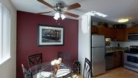 This single-floor residence offers a thoughtfully designed layout that balances style and functionality. The dining area makes a strong visual statement with its deep burgundy accent wall, creating a warm and intimate atmosphere. A ceiling fan with a built-in light fixture anchors the space, adding both practicality and charm. The round glass-top dining table, paired with elegant black metal chairs, provides a refined yet casual setting for meals and gatherings. A framed wall print adds a curated artistic touch to the room.

The dining area flows seamlessly into the kitchen, which features warm wood cabinetry and a stainless steel refrigerator that lends a modern, clean aesthetic. A skylight overhead bathes the transitional space in natural light, brightening the interior and highlighting the hardwood flooring that runs throughout. The open connection between the dining and kitchen areas creates an easy, functional flow ideal for both everyday living and hosting guests. Together, the spaces combine bold color choices, natural light, and quality finishes to create a cohesive and inviting home environment.