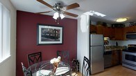 This single-floor residence offers a thoughtfully designed layout that balances style and functionality. The dining area makes a strong visual statement with its deep burgundy accent wall, creating a warm and intimate atmosphere. A ceiling fan with a built-in light fixture anchors the space, adding both practicality and charm. The round glass-top dining table, paired with elegant black metal chairs, provides a refined yet casual setting for meals and gatherings. A framed wall print adds a curated artistic touch to the room.

The dining area flows seamlessly into the kitchen, which features warm wood cabinetry and a stainless steel refrigerator that lends a modern, clean aesthetic. A skylight overhead bathes the transitional space in natural light, brightening the interior and highlighting the hardwood flooring that runs throughout. The open connection between the dining and kitchen areas creates an easy, functional flow ideal for both everyday living and hosting guests. Together, the spaces combine bold color choices, natural light, and quality finishes to create a cohesive and inviting home environment.