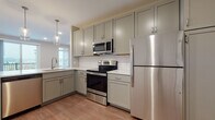 This single-floor unit offers a well-designed layout with consistent, modern finishes throughout. The kitchen is a standout feature, equipped with sage-green shaker-style cabinetry extending to the ceiling, a classic white subway tile backsplash, and a full suite of stainless steel appliances including an electric range, over-the-range microwave, and refrigerator. Warm hardwood-style flooring runs throughout the kitchen, and pendant lighting adds a polished touch above the breakfast bar, which opens directly to the living area.

The living space is generously proportioned, featuring recessed lighting, hardwood-style flooring, and a sliding glass door that opens to a private balcony with outdoor views. A secondary room with the same flooring provides flexible use as a den or office.

Bedrooms are carpeted for comfort and feature recessed lighting, ample natural light from multiple windows, and closet access. The bathroom is finished with white subway tile surrounding a full soaking tub and shower combination, complemented by a shaker-style vanity and brushed nickel fixtures. Neutral wall tones and clean white trim unify the space throughout, creating a cohesive and contemporary aesthetic.