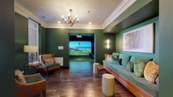 This upscale amenity space is thoughtfully designed across a single floor, combining recreation, productivity, and comfort in a cohesive, elegantly appointed environment. Rich hunter green walls, warm wood-look tile flooring, and crisp crown molding establish a refined aesthetic throughout.

The centerpiece of the recreational area is a dedicated golf simulator room, outfitted with a high-definition projection screen, a synthetic turf hitting mat, and large windows that fill the space with natural light. An adjacent lounge area provides comfortable seating with a teal built-in sofa accented by colorful throw pillows, a sculptural orb chandelier, and curated wall art — creating an inviting space to relax before or after play.

The business center features a row of computer workstations set against a dramatic framed marble-look wall panel, bathed in natural light from oversized windows. A pendant chandelier and bar-height seating complete the functional yet stylish setup.

The conference room is a standout professional space, anchored by a substantial live-edge wood table surrounded by plush grey executive chairs. A linear chandelier with cascading crystal-like elements hangs overhead, while large-scale abstract artwork adorns the walls alongside a wall-mounted display screen, making it ideal for meetings and presentations.

Connecting hallways and transition areas continue the green color palette, with tufted bar stools and additional art accents rounding out this well-appointed community amenity suite.