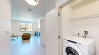Located at 345 Lincoln Ave in Amherst, MA, this modern studio unit offers a thoughtfully designed open-concept layout that maximizes every square foot. Light wood-tone flooring runs throughout, complementing the bright white walls and contemporary flush-mount lighting that keep the space feeling clean and airy.

The kitchen is a standout feature, boasting a full suite of stainless steel appliances — including a Whirlpool electric range, over-the-range microwave, dishwasher, and a full-size refrigerator. Two-tone cabinetry pairs crisp white uppers with textured gray-blue lower cabinets, all topped with a clean white countertop and accented by a sleek matte black sink faucet and hardware.

The open living and sleeping area benefits from a large window that invites natural light and offers views of the surrounding neighborhood. The space comfortably accommodates a bed, seating area with a sofa, a round coffee table, and a desk, making it both functional and livable.

A dedicated closet provides organized storage, while a discreetly tucked in-unit Whirlpool washer/dryer adds everyday convenience. The full bathroom features light wood-look flooring, a floating dark wood vanity with a white countertop, a large mirror, and chrome grab bars, reflecting a modern and accessible design aesthetic throughout.