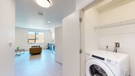 Located at 345 Lincoln Ave in Amherst, MA, this modern studio unit offers a thoughtfully designed open-concept layout that maximizes every square foot. Light wood-tone flooring runs throughout, complementing the bright white walls and contemporary flush-mount lighting that keep the space feeling clean and airy.

The kitchen is a standout feature, boasting a full suite of stainless steel appliances — including a Whirlpool electric range, over-the-range microwave, dishwasher, and a full-size refrigerator. Two-tone cabinetry pairs crisp white uppers with textured gray-blue lower cabinets, all topped with a clean white countertop and accented by a sleek matte black sink faucet and hardware.

The open living and sleeping area benefits from a large window that invites natural light and offers views of the surrounding neighborhood. The space comfortably accommodates a bed, seating area with a sofa, a round coffee table, and a desk, making it both functional and livable.

A dedicated closet provides organized storage, while a discreetly tucked in-unit Whirlpool washer/dryer adds everyday convenience. The full bathroom features light wood-look flooring, a floating dark wood vanity with a white countertop, a large mirror, and chrome grab bars, reflecting a modern and accessible design aesthetic throughout.