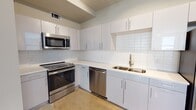This well-appointed single-floor unit showcases a cohesive modern aesthetic defined by polished concrete floors, bold dark door frames, and crisp white walls throughout. The open layout connects a spacious living area to the rest of the unit, with multiple windows fitted with blinds that draw in generous natural light across every room.

The kitchen is a standout feature, outfitted with sleek white cabinetry, white quartz countertops, and a classic subway tile backsplash. A full suite of stainless steel appliances includes an electric range, built-in microwave, dishwasher, and refrigerator, all complemented by a double-basin sink with a modern faucet. Abundant upper and lower cabinet storage adds to the kitchen's practicality.

The bedrooms are bright and well-sized, each benefiting from multiple windows that provide natural light and views of the surrounding area. One bedroom features a ceiling fan for added comfort. The hallway connects the rooms with clean, uninterrupted sightlines, reinforcing the unit's open and airy feel.

The bathroom is finished in a contemporary style with white subway tile surrounding the tub-shower combination, a white vanity with an undermount sink, quartz countertop, and wood-look flooring. Every detail of this unit reflects a thoughtfully modern design sensibility.