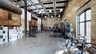 The fitness center at Germantown Mill Lofts showcases the building's rich industrial heritage through its striking architectural details. Soaring ceilings reveal exposed steel beams, visible ductwork, and original structural columns, all complemented by warm, exposed brick walls that span the length of the space. Natural light filters in through upper-level windows, brightening the polished concrete floors below and highlighting the room's generous, open layout.

The facility is well-equipped with a broad range of workout equipment, including stationary bikes, a cable machine, weight benches, a power rack with barbells and weight plates, medicine balls, and cardio machines. The equipment is thoughtfully arranged throughout the expansive floor plan, allowing ample space for movement and exercise. Pendant lighting is suspended from the ceiling at varying heights, providing both functional illumination and a design element that enhances the loft-style aesthetic.

The overall ambiance blends the raw character of a historic mill building with a functional, modern fitness environment, making it a distinctive and well-appointed amenity for residents of Germantown Mill Lofts.