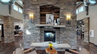 Located at 4801 Signal Tree Dr in Fort Collins, Colorado, this single-story clubhouse blends rustic mountain character with modern amenities. The entry foyer welcomes visitors with polished concrete floors, soaring ceiling heights, and glass-paneled black-framed doors that connect to the main gathering areas.

The centerpiece of the main lounge is a striking floor-to-ceiling stone fireplace wall, featuring a natural stone mantle, reclaimed wood accent niche, and flanking wall sconces that create a warm, inviting focal point. Exposed wooden beam trusses run overhead, adding to the rustic-contemporary aesthetic. A large wall-mounted smart display, leather sectional seating, and a live-edge wood coffee table furnish the lounge, while a row of windows offers views of the outdoor amenity area.

A billiard room adds recreational space, and a cozy dining nook with built-in banquette seating and an orb pendant light provides an intimate gathering spot. The kitchen area is outfitted with dark granite countertops, stainless steel appliances including a wall oven and microwave, dark cabinetry, and glass display shelving. Together, these spaces create a cohesive, upscale environment well-suited for community gatherings.