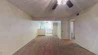 Located at 22 US Highway 60 in Canyon, Texas, this single-floor unit offers a straightforward, functional layout designed for comfortable everyday living. The main living area is generously sized, featuring wall-to-wall carpet, neutral beige walls, and a ceiling fan overhead. This space flows openly toward the kitchen, which is set slightly apart and distinguished by tile flooring, white cabinetry, a pendant light fixture, and a window that brings in natural light. The kitchen includes essential appliances and ample counter space, making it practical for daily use. Multiple additional rooms branch off from the main living area, each carpeted and equipped with ceiling fans and windows fitted with blinds, allowing for adjustable natural light. The rooms maintain a clean, neutral palette throughout, providing a blank canvas for personalization. Textured ceilings are consistent across the unit, adding a subtle detail to the interior finish. The overall layout, as seen from the 3D dollhouse view, reveals a compact yet well-organized floor plan with clear separation between the living, kitchen, and private room areas. The unit's simple design and consistent finishes make it an accessible and adaptable space situated in the small city of Canyon, Texas.