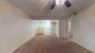 Located at 22 US Highway 60 in Canyon, Texas, this single-floor unit offers a straightforward, functional layout designed for comfortable everyday living. The main living area is generously sized, featuring wall-to-wall carpet, neutral beige walls, and a ceiling fan overhead. This space flows openly toward the kitchen, which is set slightly apart and distinguished by tile flooring, white cabinetry, a pendant light fixture, and a window that brings in natural light. The kitchen includes essential appliances and ample counter space, making it practical for daily use. Multiple additional rooms branch off from the main living area, each carpeted and equipped with ceiling fans and windows fitted with blinds, allowing for adjustable natural light. The rooms maintain a clean, neutral palette throughout, providing a blank canvas for personalization. Textured ceilings are consistent across the unit, adding a subtle detail to the interior finish. The overall layout, as seen from the 3D dollhouse view, reveals a compact yet well-organized floor plan with clear separation between the living, kitchen, and private room areas. The unit's simple design and consistent finishes make it an accessible and adaptable space situated in the small city of Canyon, Texas.