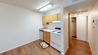 This single-floor unit offers a clean, functional layout with a cohesive design throughout. The open living area is finished with warm-toned hardwood-style flooring that extends seamlessly across the main spaces, creating a sense of continuity and warmth. White walls and a textured ceiling complement the bright, neutral palette, keeping the space feeling open and easy to personalize.

The kitchen is efficiently designed and positioned adjacent to the living area. It features light wood cabinetry with ample storage, a white electric range, a stainless steel dishwasher, and a single-basin sink. Under-cabinet range ventilation and overhead fluorescent lighting ensure the workspace is well-lit and practical. A hallway connects the kitchen to the rest of the unit, where a closet provides additional storage.

The bedroom is a well-proportioned, quiet retreat with the same warm hardwood-style flooring, a textured ceiling, and a window that allows natural light to filter in, brightening the room throughout the day.

The bathroom is appointed with large-format neutral stone-look tile surrounding the bathtub, giving the space a clean, polished appearance. The tiling extends fully around the tub surround, offering both durability and a refined aesthetic. Overall, the unit presents a straightforward, well-maintained interior suited for comfortable everyday living.