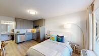 Located at 2070 McMillan Ave in North Charleston, SC, this thoughtfully designed unit maximizes every inch of its compact footprint. The open-concept layout seamlessly integrates the sleeping area with a fully equipped kitchen, creating a functional and cohesive living space. The kitchen features stainless steel appliances — including a refrigerator, microwave, and dishwasher — complemented by gray flat-front cabinetry that extends to the ceiling for ample storage and a white subway tile backsplash with an undermount sink.

The sleeping area is bright and airy, with light wood-look flooring that flows throughout the entire unit, white walls, and a large window that allows natural light to fill the room. A built-in wall shelving system with a dedicated desk area provides a practical workspace, making the unit well-suited for remote work or study.

A vestibule area near the entry serves as a transitional space, offering a closet with hanging rod and overhead shelving alongside a granite-topped vanity counter. The full bathroom is cleanly finished with a granite vanity, framed mirror, and a tub/shower combination with a curtain enclosure, all set against light wood flooring and crisp white walls. The unit's efficient design, modern finishes, and practical storage solutions make it a well-appointed and functional living space.