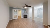 Located at 101 Shore Lake Dr in Greensboro, NC, this single-floor residence offers a well-designed layout with a clean, modern aesthetic throughout. The open living area features light hardwood-style flooring, crown molding, a ceiling fan, and a corner fireplace that serves as a focal point, creating a warm and inviting atmosphere. French doors connect the living space to an adjacent room, enhancing the open flow of the floor plan.

The kitchen is thoughtfully appointed with white shaker-style cabinetry, light stone countertops, a subway tile backsplash, and stainless steel appliances including a refrigerator, range, and microwave. An elegant orb chandelier adds a stylish finishing touch. Light hardwood-style flooring continues through this space.

The bedrooms offer comfortable carpeted flooring. One bedroom features charming arched windows that bring in ample natural light and views of the surrounding greenery, while another includes built-in corner shelving for added functionality.

The bathroom is bright and clean, showcasing light wood-style flooring, a white vanity with modern hardware, a large mirror with overhead lighting, and wainscoting along the lower walls. A dedicated in-unit laundry area houses a full-size GE washer and dryer with overhead wire shelving for storage.