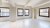 Located in the heart of downtown Detroit at 10 Witherell St, this single-floor unit offers a well-organized open-concept layout that maximizes every square foot. The combined dining room, kitchen, and living area forms the centerpiece of the space, bathed in natural light streaming through multiple dark-framed windows that frame views of the surrounding cityscape.

The kitchen is a standout feature, outfitted with warm maple cabinetry, dark granite countertops, and a full suite of stainless steel appliances including a range, microwave, and a full-size side-by-side refrigerator. A central island with a dark countertop and modern bar stools serves as both a prep space and casual dining area, seamlessly connecting the kitchen to the open living and dining zone.

The living area extends generously from the kitchen, with light-toned large-format tile flooring running throughout the entire unit, complemented by white walls and exposed ceiling beams that add architectural character. The bathroom features a clean, modern design with a wall-mounted vanity with a vessel-style sink, a walk-in glass-enclosed shower, and tile flooring. The unit is further enhanced by the convenience of in-unit laundry and a dedicated closet for storage.
