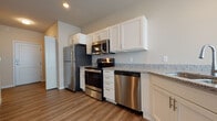 Located at 1805 Parmenter St in Middleton, Wisconsin, this single-floor unit offers a clean, contemporary design with consistent finishes throughout. The kitchen is a standout feature, equipped with a full suite of stainless steel appliances including a refrigerator, electric range, built-in microwave, and dishwasher. White shaker-style cabinetry provides generous storage, complemented by granite-look countertops and a peninsula that opens toward the living area. A pendant light fixture accents the peninsula, reinforcing the open, connected layout between the kitchen and main living space.

Wood-style plank flooring runs throughout the unit, lending warmth and visual continuity from room to room. The living area is bright and open, with large windows fitted with blinds that allow for natural light while maintaining privacy. Vaulted ceiling lines add a sense of vertical space to select areas of the unit.

The bedroom features dual windows with a wall-mounted PTAC climate control unit, ensuring year-round comfort. Neutral warm-toned walls provide a calm, livable atmosphere. The bathroom includes a tub/shower combination, a white vanity with granite-style countertop, and wood-style flooring, maintaining the cohesive aesthetic found throughout the rest of the space.