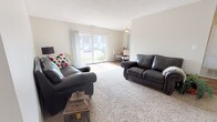 This upgraded single-floor residence in Canton, Michigan offers a well-organized layout with two bedrooms and one full bathroom. The living room is generously sized, featuring plush wall-to-wall carpeting, a textured ceiling, and a sliding glass door that fills the space with natural light while providing direct outdoor views. The open flow connects the living area to a dedicated dining space, where a large window overlooks lush greenery, creating a bright and inviting atmosphere for meals.

The galley-style kitchen is thoughtfully appointed with warm wood cabinetry, light laminate countertops, wood-look flooring, and a full suite of appliances including a dishwasher and refrigerator. A window above the sink brings in additional natural light. The kitchen connects conveniently to the main entry door.

Both bedrooms are carpeted and well-lit, each featuring vertical blinds on multiple windows that allow for flexible light control. One bedroom offers versatility as a guest room or home office. The full bathroom includes a single-sink vanity with wood cabinetry, a tub/shower combination, and wood-look flooring, providing a clean and functional finish throughout.