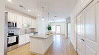 Located at 12020 Brush Hill Rd in Wildwood, FL, this well-designed one-bedroom, one-bathroom residence offers a thoughtfully efficient layout across a single floor. The open-concept living and kitchen area serves as the heart of the home, where light wood-look flooring, white walls, and recessed lighting create a clean, airy atmosphere. The kitchen is a standout feature, showcasing white shaker cabinetry, granite countertops, a central island with pendant lighting, and a full suite of stainless steel appliances including a French door refrigerator, range, microwave, and dishwasher. The kitchen flows seamlessly into the living room, which benefits from natural light streaming through windows and a glass-paneled door, complemented by a ceiling fan overhead. The bedroom is a calm, carpeted retreat featuring a ceiling fan, a window with blinds, and direct access to a dedicated closet equipped with wire shelving for organized storage. The full bathroom is well-appointed with a granite-topped vanity, white cabinetry, a large framed mirror, and a tiled tub-shower combination. Throughout the space, the consistent use of neutral tones, modern fixtures, and quality finishes creates a cohesive and comfortable living environment.