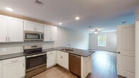 Located at 29568 Brant Ct in Easton, Maryland, this single-floor residence offers a clean, modern layout designed for comfortable everyday living. The open-concept kitchen and living area forms the heart of the home, where wood-look flooring flows seamlessly throughout. The kitchen is outfitted with white shaker-style cabinetry, dark granite-style countertops, and a full suite of stainless steel GE appliances, including a refrigerator, electric range, over-the-range microwave, and dishwasher. A peninsula with an integrated sink adds both prep space and a natural divider between the kitchen and the adjoining living area, which is brightened by a window overlooking greenery outside. The bedrooms feature plush carpeting and ceiling fans with light fixtures, providing a comfortable retreat. One bedroom includes a private en-suite bathroom, while an additional full bathroom serves the rest of the home. Both bathrooms are finished with wood-look flooring, white vanities, and clean, modern fixtures. A dedicated laundry room houses a full-size top-load washer and dryer alongside overhead shelving for added storage. Throughout the home, neutral tones and recessed lighting create a bright, welcoming ambiance.