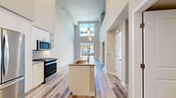 Located at 1774 Metro Avenue in Chula Vista, CA, this modern two-story residence offers 790 square feet of thoughtfully designed living space, featuring 1 bedroom and 2 bathrooms across two floors (610 sq ft on the ground floor and 180 sq ft on the upper level). Throughout the unit, light-toned wood-style flooring creates a cohesive, contemporary aesthetic. The living room is a standout architectural feature, boasting soaring double-height ceilings, floor-to-ceiling glass doors with black metal frames, and a transom window above that floods the space with abundant natural light and provides views of the surrounding streetscape. The kitchen and living room share an open-concept layout, with the kitchen showcasing white shaker cabinetry, grey quartz countertops, a herringbone tile backsplash, and stainless steel appliances including a gas range, over-the-range microwave, and French door refrigerator. The bedroom, approximately 100 square feet, features a sliding closet with paneled doors and a large window with neighborhood views. Both bathrooms are finished with white cabinetry, grey countertops, and wood-style flooring; one includes a full soaking tub and shower combination, while the other features a louvered closet and built-in open shelving.