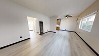 Located at 625 N State St in Ukiah, California, this 2-bedroom, 1-bathroom residence offers a practical and well-appointed single-floor layout. Light vinyl plank flooring runs throughout the entire unit, creating a clean, cohesive look from room to room. The open living area is bright and welcoming, featuring a ceiling fan, textured ceiling, and a window with an in-wall air conditioning unit that allows natural light to fill the space. The galley-style kitchen is efficiently designed with warm wood cabinetry lining both sides, ample counter space, a double-basin sink with a black matte faucet, and white appliances including a range and refrigerator. The spacious primary bedroom comfortably accommodates larger furnishings and includes a ceiling fan and a wide open closet with a full-width hanging rod. The second bedroom also features a ceiling fan and a window, offering a versatile space suitable for a guest room or home office. The bathroom is clean and functional, with a full-sized tub and shower combination finished in classic white subway tile. A hallway connects the rooms efficiently, and the unit includes an additional closet for extra storage. Bold black baseboards throughout provide a modern contrast to the neutral white walls.