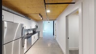 Located at 701 Easley Bridge Rd in Greenville, SC, this two-story industrial-modern space masterfully blends raw architectural character with contemporary finishes. The lower level features polished concrete floors that stretch throughout, complemented by warm wood-planked ceilings with exposed ductwork and track lighting that highlight the space's industrial roots. The fully equipped kitchen is a standout feature, outfitted with sleek white cabinetry, black hardware, dark countertops, a penny-tile backsplash, and a full suite of stainless steel appliances including a refrigerator, range, microwave, and dishwasher. A half bath on the main level includes a floating white vanity with a dark countertop and matte black fixtures, finished with polished concrete flooring. An open-tread wood staircase with black metal railings leads to the upper level, where original heavy timber beams and wood-plank ceilings create a dramatic, loft-like atmosphere. The upper floor features light hardwood flooring, a bold black structural column, and windows that allow natural light to filter in. A full bathroom on this level includes a soaking tub with white subway tile surround and a matte black shower rod, paired with distinctive black-painted doors that add a striking contrast throughout.