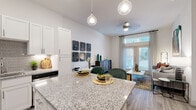 This 1-bedroom, 1-bathroom residence features a smart, efficient layout that maximizes every square foot across a single floor. The open-concept kitchen is a standout, showcasing white shaker cabinetry, granite countertops, a subway tile backsplash, stainless steel appliances, and a large island that doubles as a breakfast bar — all finished with wood-look flooring for a clean, contemporary feel. The kitchen flows seamlessly into the living area, which benefits from tall ceilings, French doors, and oversized windows that flood the space with natural light and provide outdoor views. The bedroom offers plush carpeting, a large window with exterior views, and direct access to a spacious walk-in closet complete with built-in shelving and dual hanging rods for ample storage. The full bathroom connects to the bedroom and features a granite-topped vanity with white cabinetry, a soaking tub with tile surround, and wood-look flooring that ties the space together. Neutral wall tones and consistent high-quality finishes throughout create a cohesive, bright, and inviting ambiance well-suited for comfortable everyday living.