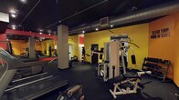 This single-floor fitness facility offers a comprehensive workout environment designed to accommodate a variety of training needs. The space is immediately defined by its striking interior palette — vivid yellow walls contrast sharply against a dark, exposed black ceiling, creating an energetic and motivating atmosphere. Industrial-style ductwork and track lighting run overhead, providing focused illumination throughout the workout floor.

The space is equipped with a diverse selection of strength training machines, including a multi-function cable and weight stack system, an adjustable bench press station, and various resistance machines suited for both upper and lower body workouts. A dedicated free weights area lines one wall, with a full-length mirror allowing for form checks during exercises. Dumbbells and weight racks are neatly arranged alongside cardio equipment, including treadmills visible toward the front of the space.

Rubber flooring covers the entire workout area, providing durability and safety underfoot. Structural columns are integrated into the layout, subtly dividing the floor into functional training zones without disrupting the open feel. The overall design is utilitarian yet purposeful, offering a no-frills, high-function environment built entirely around athletic performance and training efficiency.