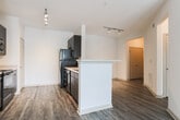 Located in Lawrenceville, GA, this single-floor residence offers a well-designed open-concept layout that seamlessly connects the living, dining, and kitchen areas. Rich, dark-toned hardwood-style flooring runs throughout the entire space, adding warmth and visual continuity from room to room.

The kitchen is a functional centerpiece, featuring dark espresso cabinetry, light-colored countertops, a tiled backsplash, and a full suite of black appliances including a refrigerator, stove, microwave, and dishwasher. A peninsula counter with a raised bar edge defines the kitchen boundary and provides additional prep or casual dining space.

The living area is generously sized and bathed in natural light from a large picture window and a glass door that opens directly to a private outdoor balcony or patio, offering pleasant exterior views. Track lighting in the main living and kitchen areas provides modern, adjustable illumination.

The bedroom is a comfortable retreat equipped with a ceiling fan, a walk-in closet with built-in shelving, and direct access to the bathroom. The bathroom includes a full-sized soaking tub with a shower, white tile surround, and chrome fixtures, maintaining a clean and functional aesthetic throughout. The overall ambiance of this space is bright, clean, and move-in ready.