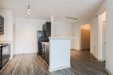Located in Lawrenceville, GA, this single-floor residence offers a well-designed open-concept layout that seamlessly connects the living, dining, and kitchen areas. Rich, dark-toned hardwood-style flooring runs throughout the entire space, adding warmth and visual continuity from room to room.

The kitchen is a functional centerpiece, featuring dark espresso cabinetry, light-colored countertops, a tiled backsplash, and a full suite of black appliances including a refrigerator, stove, microwave, and dishwasher. A peninsula counter with a raised bar edge defines the kitchen boundary and provides additional prep or casual dining space.

The living area is generously sized and bathed in natural light from a large picture window and a glass door that opens directly to a private outdoor balcony or patio, offering pleasant exterior views. Track lighting in the main living and kitchen areas provides modern, adjustable illumination.

The bedroom is a comfortable retreat equipped with a ceiling fan, a walk-in closet with built-in shelving, and direct access to the bathroom. The bathroom includes a full-sized soaking tub with a shower, white tile surround, and chrome fixtures, maintaining a clean and functional aesthetic throughout. The overall ambiance of this space is bright, clean, and move-in ready.