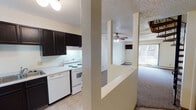 Located at 415 W Century Ave in Bismarck, North Dakota, this two-floor residential unit offers a practical and well-organized layout. The kitchen is a standout functional space, featuring dark cabinetry that contrasts with white appliances, including an electric range, dishwasher, and refrigerator. Light-colored countertops and tile flooring complete the kitchen, which is partially separated from the adjoining areas by a structural column and half-wall partition, allowing for an open, connected feel. The entry hallway provides a smooth transition from the front door into the main living areas, with tile flooring that extends from the kitchen into the entry zone. The living area is generously sized, finished with neutral carpet and equipped with a ceiling fan and a wall-mounted air conditioning unit. A sliding glass door allows natural light to filter into the living space. The bedrooms are carpeted and feature vertical blinds over windows, baseboard heating, and wall-mounted air conditioning units, providing year-round comfort. The bathroom presents a clean, utilitarian design with tile flooring, a single-sink vanity with dark cabinetry, and ample space. Textured ceilings are consistent throughout, contributing to the unit's cohesive interior character.