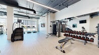 Located at 8521 Sepulveda Blvd in Los Angeles, this fitness center offers a generously sized, single-floor workout space designed with a modern industrial aesthetic. The open layout features exposed ductwork and structural elements against a clean white ceiling, complemented by light wood-style flooring that creates a bright, energetic atmosphere throughout.

Large floor-to-ceiling windows line portions of the perimeter, flooding the space with abundant natural light and offering views of the surrounding Westchester neighborhood. A dedicated cardio zone near the windows houses a row of treadmills and elliptical machines, allowing members to work out with an inspiring outdoor backdrop. A stair climber adds further variety to the cardio offerings.

The strength training area is well-appointed with a multi-functional cable machine, a full rack of dumbbells neatly arranged along a mirrored wall, and adjustable weight benches. The mirrors enhance the sense of spaciousness while providing essential visual feedback during workouts.

A standout feature is a bold, colorful motivational mural that spans an entire wall, featuring vibrant typography and imagery, including an iconic "You've Got This" message, palm trees, and a sunburst design that energizes the space with a distinctly Los Angeles spirit. The overall design balances functionality with an uplifting, community-oriented ambiance suited to a wide range of fitness activities.