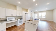 This thoughtfully designed single-floor unit offers a bright, open layout that maximizes functionality and comfort. The combined kitchen and living area serves as the heart of the home, showcasing a central island with a granite countertop and undermount sink — an ideal spot for casual dining or food preparation. The kitchen is equipped with white shaker-style cabinetry, matching granite countertops, a full suite of white GE appliances including an electric range, refrigerator, and microwave, as well as a dedicated built-in desk nook. Warm hardwood-style flooring flows seamlessly throughout the entire unit, adding a cohesive and inviting feel. The living area benefits from natural light streaming through large windows, creating an airy and open ambiance. The bedroom is a comfortable retreat, featuring a ceiling fan, a generous window with outdoor views, and access to a dedicated closet. The bathroom continues the granite and white cabinetry theme, offering a clean, modern aesthetic. Additional conveniences include an in-unit laundry area. Recessed lighting throughout the unit ensures well-lit spaces at every hour of the day.