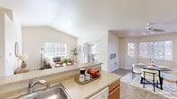 Located in Liberty Lake, WA, this 2-bedroom, 1-bathroom residence offers a thoughtfully designed single-floor layout. The open-concept living, dining, and kitchen area serves as the heart of the home, distinguished by soaring vaulted ceilings that amplify the sense of space. Large windows flood the living room with natural light, while a private balcony extends the living space outdoors. The galley-style kitchen features warm honey-toned cabinetry, light countertops, white appliances including a range, microwave, refrigerator, and dishwasher, and ample storage. The adjacent dining area is brightened by a window with views of the surrounding greenery. Both bedrooms are carpeted and well-lit, with the primary bedroom offering generous proportions and a closet. The second bedroom also benefits from natural light through large windows. The bathroom includes a full tub-shower combination, a wood-toned vanity with a single sink, and a large mirror. Wood-look flooring runs throughout the main living areas, tying the space together cohesively. Four closets throughout the unit provide abundant storage, completing this well-appointed and comfortable residence.