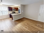Located at 6133 Edward St, Unit 202 in Norfolk, VA, this single-floor apartment offers 3 bedrooms, 2 bathrooms, and 680 square feet of thoughtfully arranged living space. The open kitchen and living room area serves as the heart of the unit, featuring rich dark wood cabinetry, light granite-style countertops, stainless steel appliances including a gas range, microwave, refrigerator, and dishwasher, and a peninsula with an integrated sink. Wood-look laminate flooring runs throughout the kitchen and living areas, complemented by a large window that brings in natural light. The three bedrooms are carpeted in warm beige tones, with neutral-painted walls and textured ceilings. The primary bedroom measures 220 square feet, offering ample space. Bedrooms are served by two full bathrooms — one featuring a white-tiled soaking tub/shower combo, and the other with a dark wood vanity, white countertop, and a well-lit mirror with a multi-bulb light fixture. A hallway connects the rooms, providing a functional layout. White panel doors and clean white trim are consistent throughout, contributing to a cohesive and neutral aesthetic well-suited for any décor style.