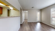 This single-floor unit is designed with a practical, open layout that connects the main living areas seamlessly. The living room serves as the centerpiece of the space, featuring wood-look flooring, a large picture window that invites natural light, and a tile-surround fireplace with built-in shelving — a notable focal point that adds character to the room. A textured ceiling is present throughout, contributing to the overall aesthetic.

The kitchen is configured in a galley style, equipped with warm-toned wood cabinetry, laminate countertops, a double sink, and white appliances including a refrigerator and range. A pass-through window connects the kitchen to the living area, enhancing the sense of openness. The living space also features a private exterior door with a window panel, providing direct outdoor access.

The bedroom offers a comfortable, neutral environment with the same wood-look flooring and access to a closet with shelving. The bathroom includes a full soaking tub and shower combination with tile surround and chrome fixtures, complemented by additional cabinetry above for storage. The unit's neutral color palette and consistent flooring throughout create a cohesive and clean aesthetic.