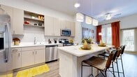 This efficiently designed one-bedroom, one-bathroom residence offers a thoughtful layout across a single floor, maximizing every square foot for comfortable everyday living. The open-concept kitchen is a standout feature, outfitted with a full suite of stainless steel appliances including a gas range, built-in microwave, dishwasher, and French door refrigerator. Taupe cabinetry with open display shelving, a white quartz countertop, and a subway tile backsplash lend a clean, modern aesthetic. A central island with bar seating provides additional prep space and casual dining. Wood-look plank flooring runs throughout the main living areas, flowing naturally into the living room, which is bathed in natural light from large windows and a glass door that opens to the outdoors. The bedroom features plush wall-to-wall carpet, a ceiling fan, and wide windows that bring in ample daylight. A dedicated closet offers convenient storage. The bathroom is finished with a single-sink vanity, white quartz countertop, and matching cabinetry, continuing the cohesive design language found throughout the residence. Recessed lighting and neutral wall tones create a bright, welcoming ambiance throughout the entire space.