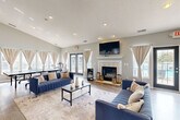 Located at 15685 Goddard Rd in Southgate, Michigan, this single-story community clubhouse offers a generously sized, thoughtfully designed gathering space for residents. The facility spans a substantial footprint across one floor, encompassing distinct functional areas that cater to relaxation, socializing, and fitness.

The main lounge is bright and open, featuring rich hardwood-style flooring, recessed lighting, and a classic white-mantled fireplace topped with a wall-mounted television. Comfortable blue sofas are arranged on a neutral area rug, creating an inviting seating area. Multiple French doors and large draped windows flood the room with natural light and provide direct views of and access to the outdoor pool area. A ping-pong table adds a recreational element to the space.

Adjacent to the lounge is a well-equipped kitchen area boasting vaulted ceilings with a skylight, white cabinetry, stainless steel appliances, and a distinctive curved island wrapped in textured tile with bar seating — ideal for casual gatherings.

The welcoming entry lobby features soaring ceilings, bold teal accent walls, and warm hardwood-style flooring, setting an energetic and modern tone upon arrival.

The fitness center is boldly designed with vibrant orange and gray walls, motivational typography, and a full suite of equipment including treadmills, an elliptical, cable machines, and a free-weight station with floor-to-ceiling mirrors.