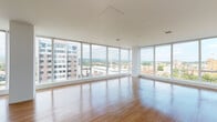 Located at 144 S Harrison St in East Orange, NJ, this modern high-rise unit offers an impressive blend of contemporary design and elevated urban living. The open living area is a standout feature, wrapped in expansive floor-to-ceiling glass windows that stretch across multiple walls, flooding the space with abundant natural light and framing sweeping panoramic views of the East Orange skyline and surrounding hillside landscape. Rich hardwood flooring runs throughout, adding warmth to the bright, airy interior. The kitchen is thoughtfully appointed with sleek white cabinetry extending to the ceiling, a mosaic tile backsplash, light stone countertops, and a full suite of stainless steel appliances including a refrigerator, range, built-in microwave, and dishwasher. A large window in the kitchen continues the theme of bringing the outdoors in. The bathroom features a clean, modern aesthetic with large-format marble-look wall tiles, a wall-mounted floating vanity with an integrated sink, a soaking tub with overhead shower, and neutral tile flooring. The overall ambiance is bright, minimalist, and sophisticated, making this an ideal urban retreat with striking views at every turn.