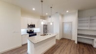 This single-story residence in Waxahachie, Texas offers a clean, contemporary design characterized by a neutral color palette, wood-look plank flooring, and recessed lighting throughout. The open-concept kitchen serves as a focal point, showcasing a large center island topped with granite countertops and an undermount sink, illuminated by elegant pendant lights. White shaker-style cabinetry extends to the ceiling, providing generous storage, while a white subway tile backsplash and a full suite of stainless steel appliances—including a refrigerator, electric range, and built-in microwave—complete the well-appointed space.

The living area is generously proportioned with high ceilings and a clean, open layout, offering a versatile canvas for furnishing. The bedroom features wood-look flooring, a ceiling fan, and a window that introduces natural light into the space.

The primary bathroom is a standout feature, finished with large-format marble-style tile flooring, a dual-sink vanity with granite countertops and framed mirrors, and a soaking tub alongside a tiled shower surround. Directly accessible from the bathroom is a spacious walk-in closet outfitted with multiple shelving tiers and hanging rods, offering substantial organizational capacity throughout.