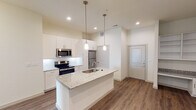 This single-story residence in Waxahachie, Texas offers a clean, contemporary design characterized by a neutral color palette, wood-look plank flooring, and recessed lighting throughout. The open-concept kitchen serves as a focal point, showcasing a large center island topped with granite countertops and an undermount sink, illuminated by elegant pendant lights. White shaker-style cabinetry extends to the ceiling, providing generous storage, while a white subway tile backsplash and a full suite of stainless steel appliances—including a refrigerator, electric range, and built-in microwave—complete the well-appointed space.

The living area is generously proportioned with high ceilings and a clean, open layout, offering a versatile canvas for furnishing. The bedroom features wood-look flooring, a ceiling fan, and a window that introduces natural light into the space.

The primary bathroom is a standout feature, finished with large-format marble-style tile flooring, a dual-sink vanity with granite countertops and framed mirrors, and a soaking tub alongside a tiled shower surround. Directly accessible from the bathroom is a spacious walk-in closet outfitted with multiple shelving tiers and hanging rods, offering substantial organizational capacity throughout.