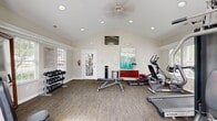 This 380 square foot fitness center, located at 6340 Saddler Way in Canal Winchester, OH, is a single-story facility designed to provide a comprehensive workout experience. The space features vaulted ceilings with recessed lighting, creating an open and airy atmosphere. Large windows and a glass door allow abundant natural light to flood the room, offering views of the surrounding greenery.

The gym is equipped with a variety of exercise machines, including treadmills, ellipticals, stationary bikes, and weight training equipment. A multi-station weight machine occupies one corner, while free weights and benches are strategically placed throughout. The room also includes a dedicated area for floor exercises, complete with exercise balls and mats.

The flooring consists of durable, low-maintenance gray carpeting, ideal for a fitness environment. White walls and trim contribute to the clean, modern aesthetic. For entertainment and instruction, a wall-mounted flat-screen TV is prominently displayed. Additional amenities include a water cooler, towel service, and informational posters outlining fitness center rules and guidelines.

The thoughtful layout maximizes the available space, allowing for efficient traffic flow between equipment stations. This well-designed fitness center provides residents with a convenient, fully-equipped facility for maintaining their health and wellness routines.