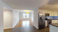 This single-floor residence offers a thoughtfully designed layout with a blend of classic architectural details and modern finishes. The open living and dining area is anchored by warm hardwood flooring that reflects natural light from dual windows, while crown molding adds a refined touch to the white-painted walls. A yellow pendant light fixture serves as a focal point, enhancing the welcoming ambiance.

The kitchen is a standout feature, showcasing white shaker-style cabinetry, dark countertops, a marble-look tile backsplash, and a full suite of stainless steel appliances including a gas range, microwave, and French door refrigerator. A central island with pendant globe lighting provides additional prep space and casual seating potential. Large-format dark tile flooring grounds the kitchen area.

The bedrooms feature gleaming hardwood floors, crown molding, soft neutral wall tones, and ample natural light through multiple windows. One bedroom includes access to a walk-in closet with built-in shelving.

Two bathrooms serve the residence. The primary bathroom offers a glass-enclosed shower, double vanity with dark cabinetry and white countertops, and large-format tile flooring. The secondary bathroom features classic penny-tile flooring, a soaking tub with mosaic tile surround, and a window for natural light.