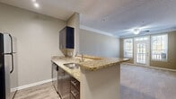 Located in Brookhaven, GA, this two-bedroom, one-bathroom residence offers a thoughtfully designed single-floor layout. The galley-style kitchen is a standout feature, showcasing granite countertops, dark espresso cabinetry, wood-look plank flooring, and stainless steel appliances including a range, microwave, and refrigerator. A peninsula with an undermount sink and extended counter space bridges the kitchen to the living area, making it ideal for both cooking and casual dining.

The living room is bright and welcoming, featuring crown molding, a textured ceiling, a ceiling fan, and plush carpet flooring. A glass-paned door opens directly to a private balcony, filling the space with natural light and outdoor views.

The primary bedroom offers a comfortable footprint with carpet flooring, a ceiling fan, and a large window that frames natural light. The second bedroom is equally well-lit, with a sizable window and soft carpet. A dedicated closet provides additional storage.

The hallway connects the bedrooms to the full bathroom, which features wood-look vinyl plank flooring, a dark-toned vanity with storage, a mirror, and a tiled shower-tub combination. The neutral warm-beige palette throughout creates a cohesive and calming ambiance across the entire residence.