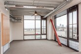 This single-floor unit showcases a distinctive industrial aesthetic, combining raw structural elements with modern finishes throughout. The open living and kitchen area is immediately striking, with exposed ductwork and concrete ceilings soaring overhead, track lighting, and floor-to-ceiling windows that flood the space with natural light and offer views of the surrounding neighborhood. Bold red structural steel columns serve as architectural accents, adding a dynamic visual element to the open layout.

The kitchen is well-appointed with light maple cabinetry, dark countertops, a tiled backsplash, and a full suite of stainless steel appliances including a range, over-the-range microwave, dishwasher, and refrigerator. A breakfast bar with a dark countertop extends from the kitchen, providing a casual dining option that connects seamlessly to the living area.

The bathroom features a clean, functional design with warm wood-toned cabinetry, dark countertops, a single basin sink, a full-size mirror, and a combined tub and shower unit with built-in shelving — all set on durable, neutral-toned flooring.

A dedicated laundry area accommodates a stacked washer and dryer unit alongside a water heater, keeping essential utilities conveniently within the unit. Neutral carpeting throughout the living spaces and soft, consistent wall tones contribute to a cohesive and comfortable overall ambiance.